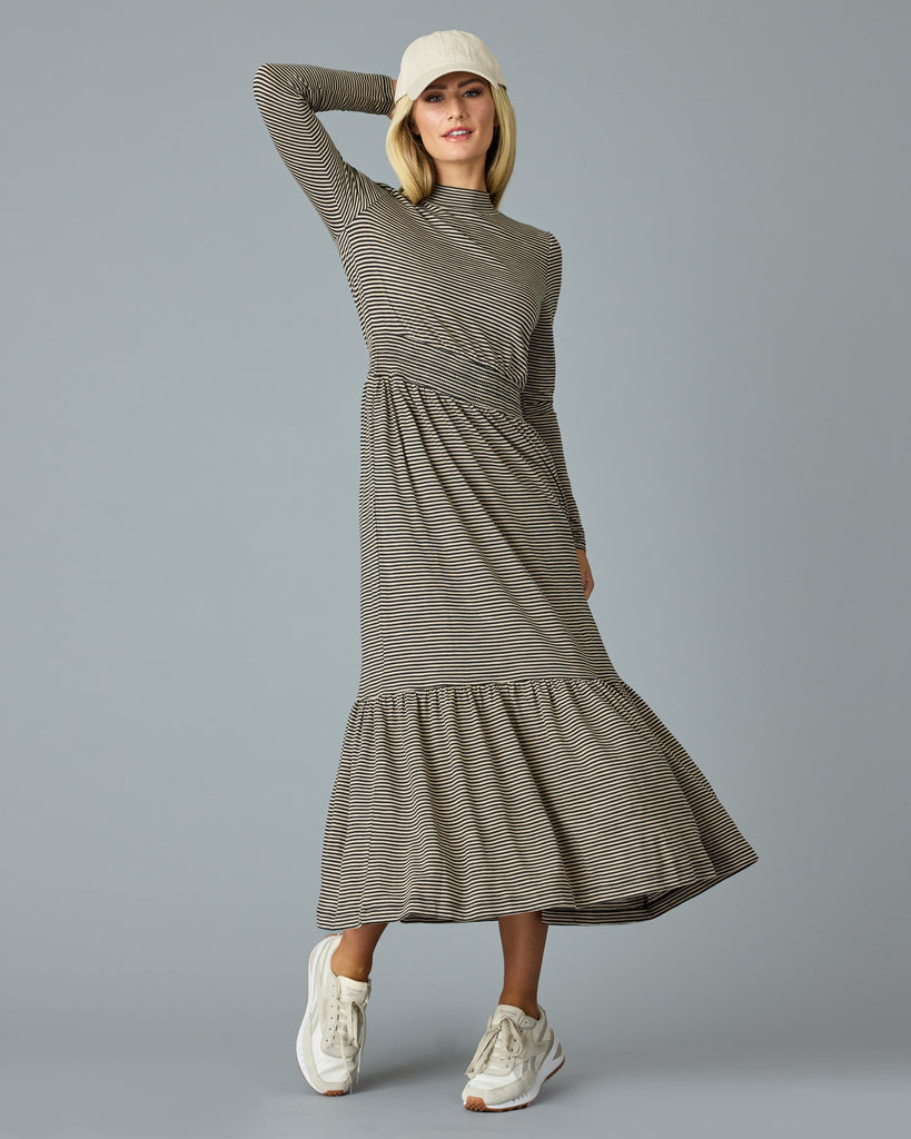 Woman in a black and tan thin striped maxi dress with long sleeves, a mock neck and pockets