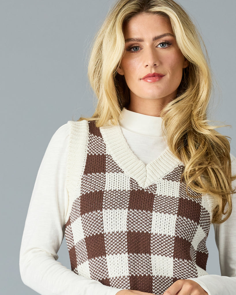 Woman in a black and white plaid v-neck sweater vest with white mock neck underneath