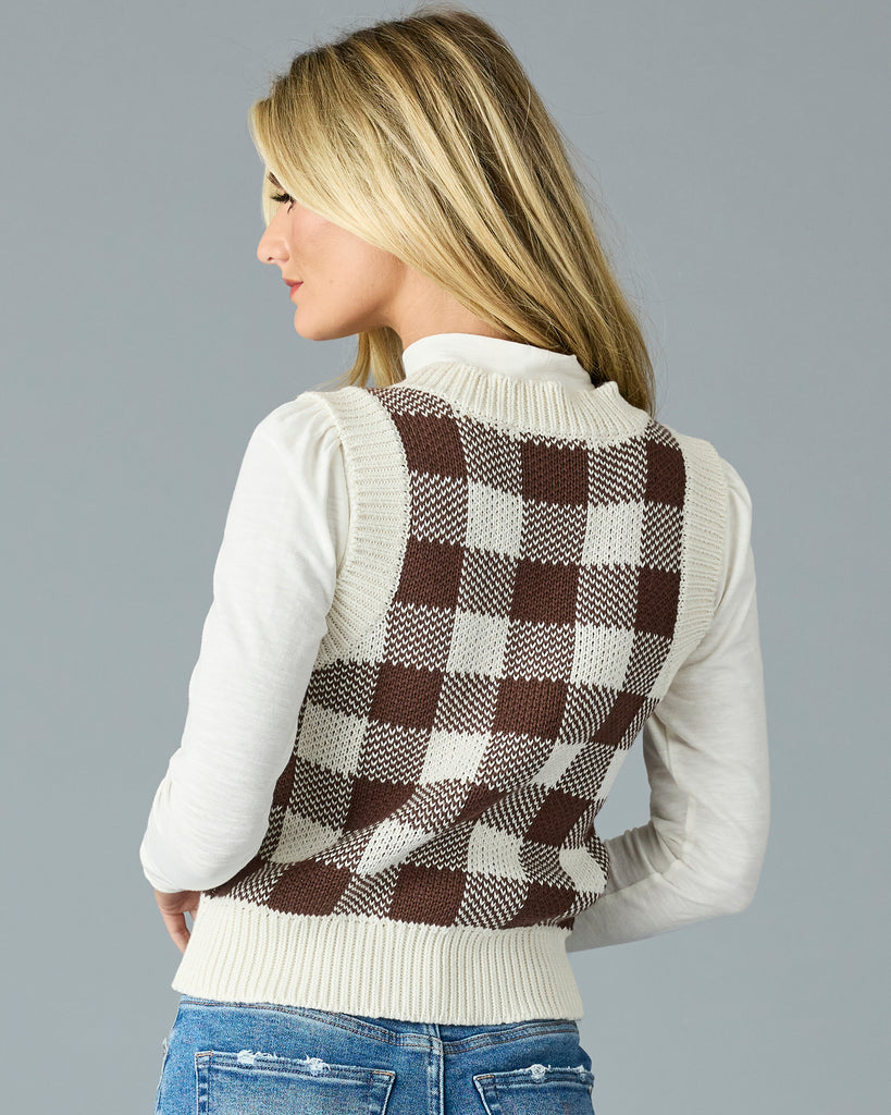 Woman in a black and white plaid v-neck sweater vest with white mock neck underneath