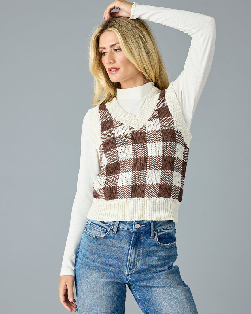 Woman in a black and white plaid v-neck sweater vest with white mock neck underneath