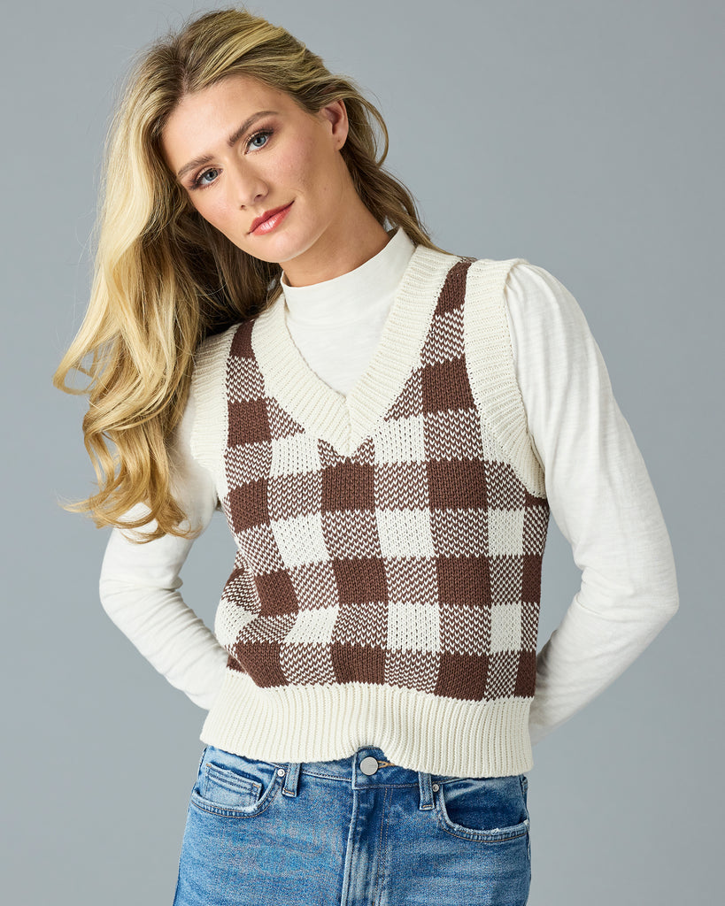 Woman in a black and white plaid v-neck sweater vest with white mock neck underneath