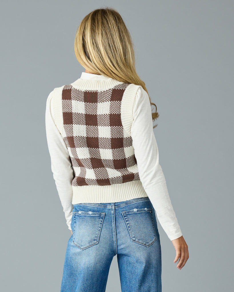 Woman in a black and white plaid v-neck sweater vest with white mock neck underneath