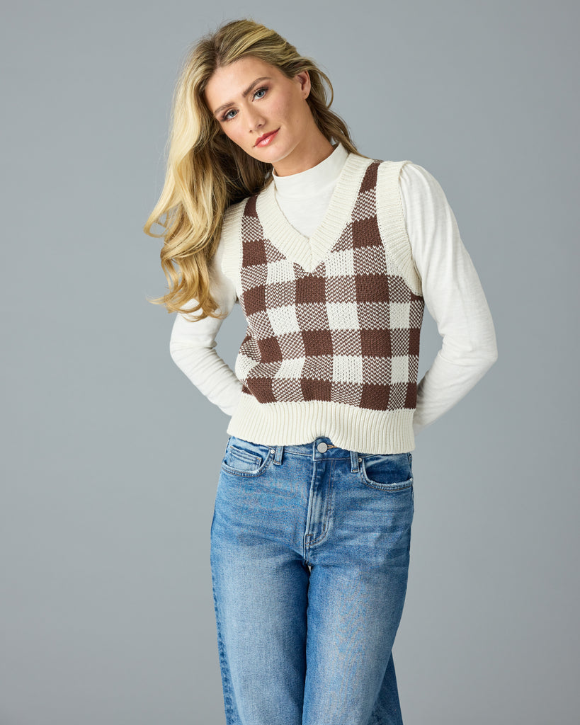 Woman in a black and white plaid v-neck sweater vest with white mock neck underneath