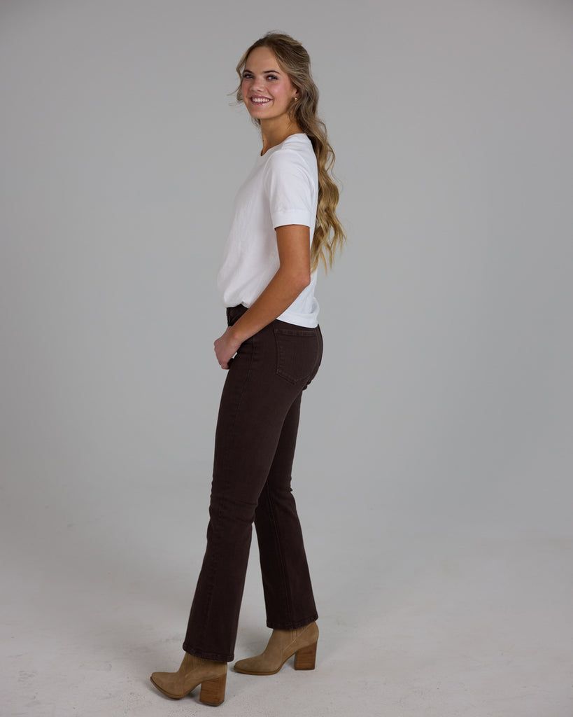 Model wearing dark brown bootcut ankle length denim jeans.