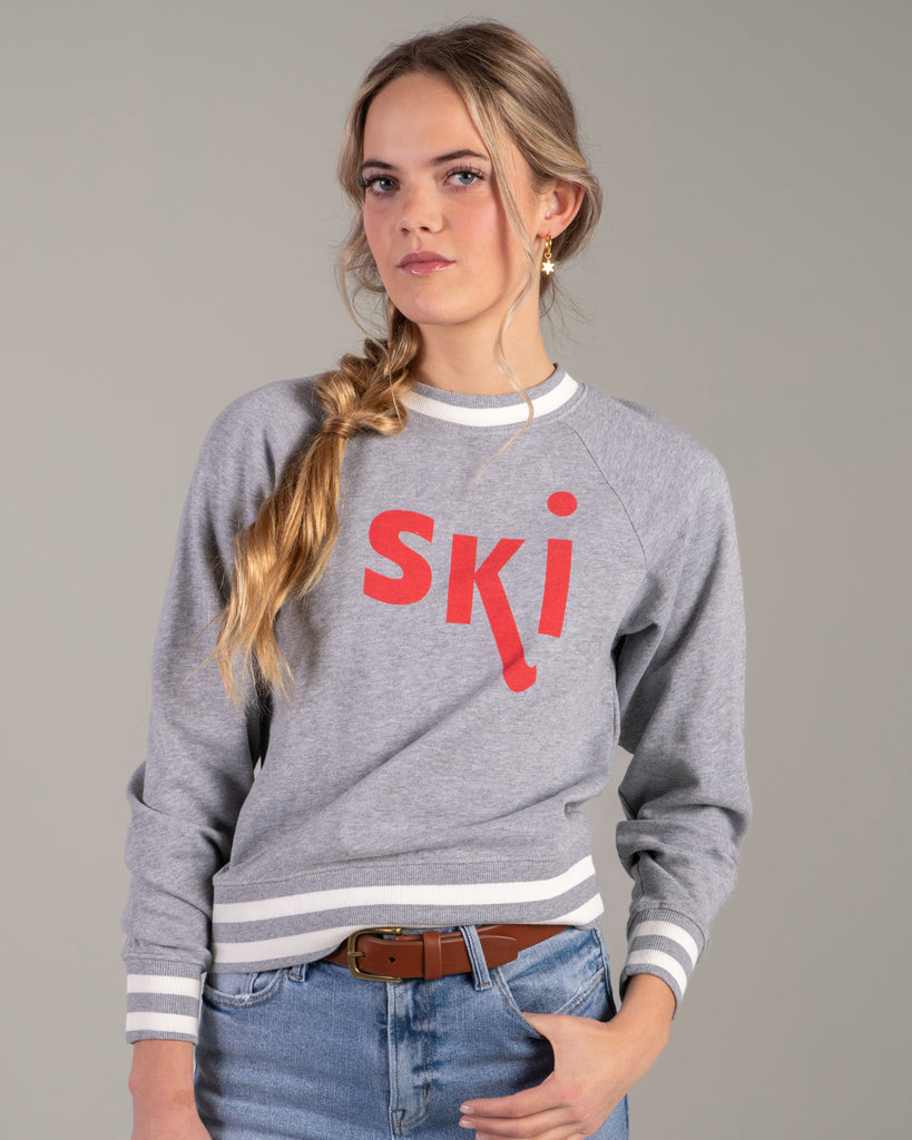 Woman in a grey pullover sweater with "ski" across the front in red lettering