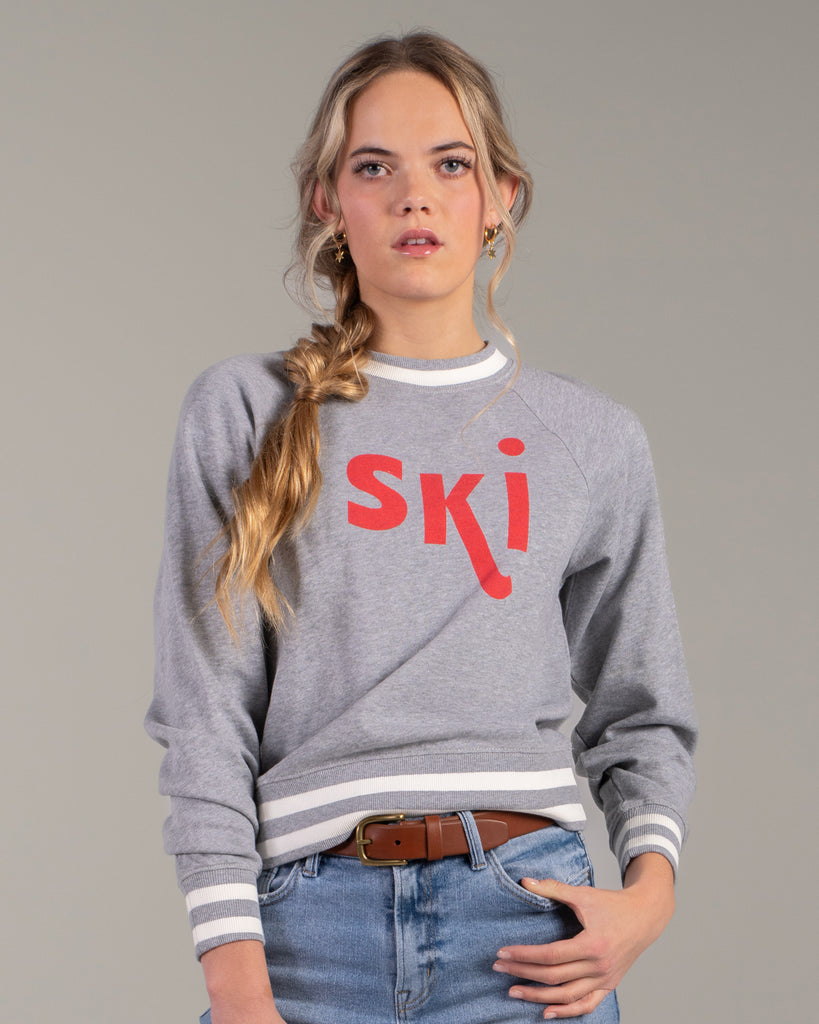 Woman in a grey pullover sweater with "ski" across the front in red lettering