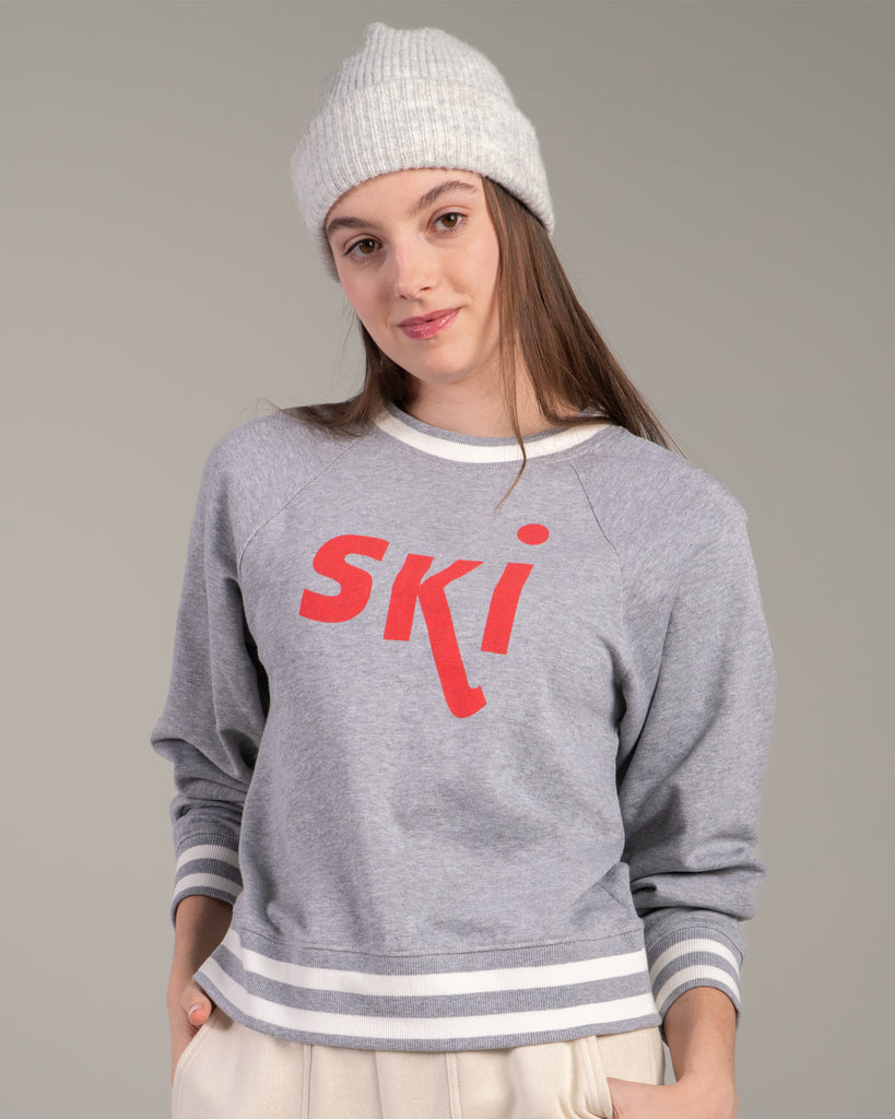 Woman in a grey pullover sweater with "ski" across the front in red lettering