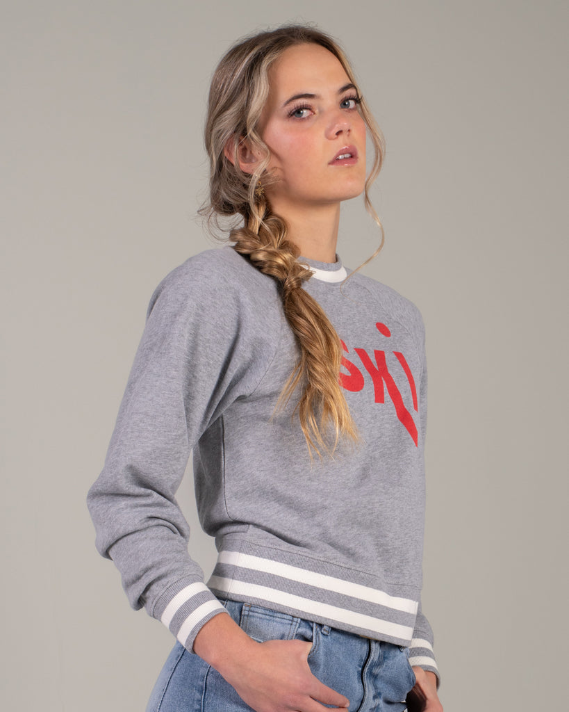 Woman in a grey pullover sweater with "ski" across the front in red lettering