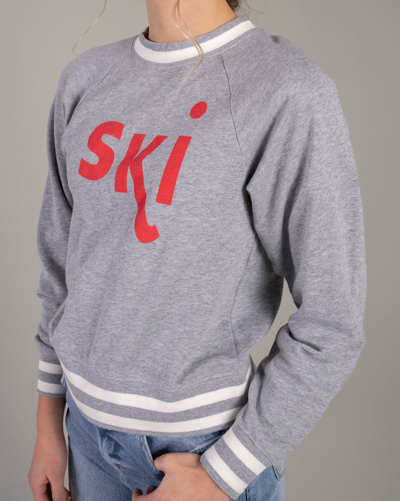 Woman in a grey pullover sweater with "ski" across the front in red lettering