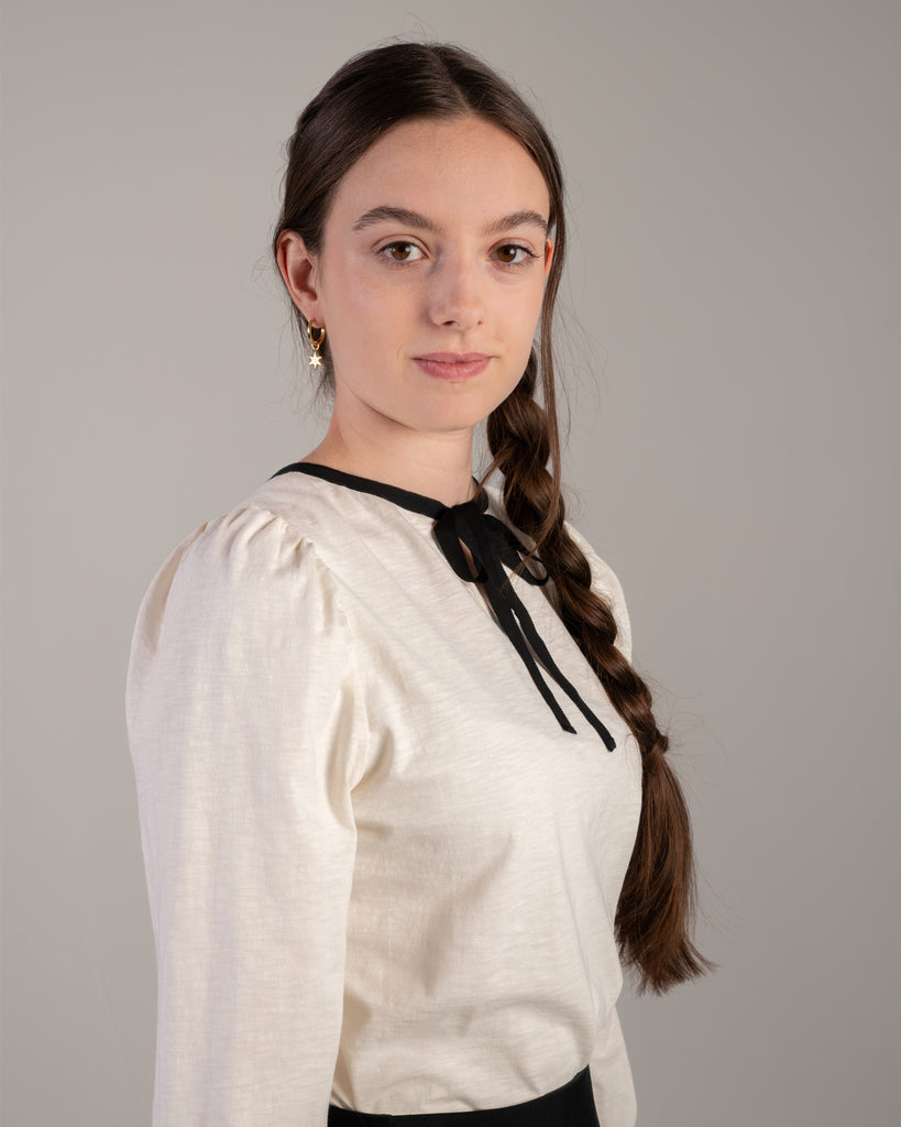 Woman in a white blouse with black detail around neckline