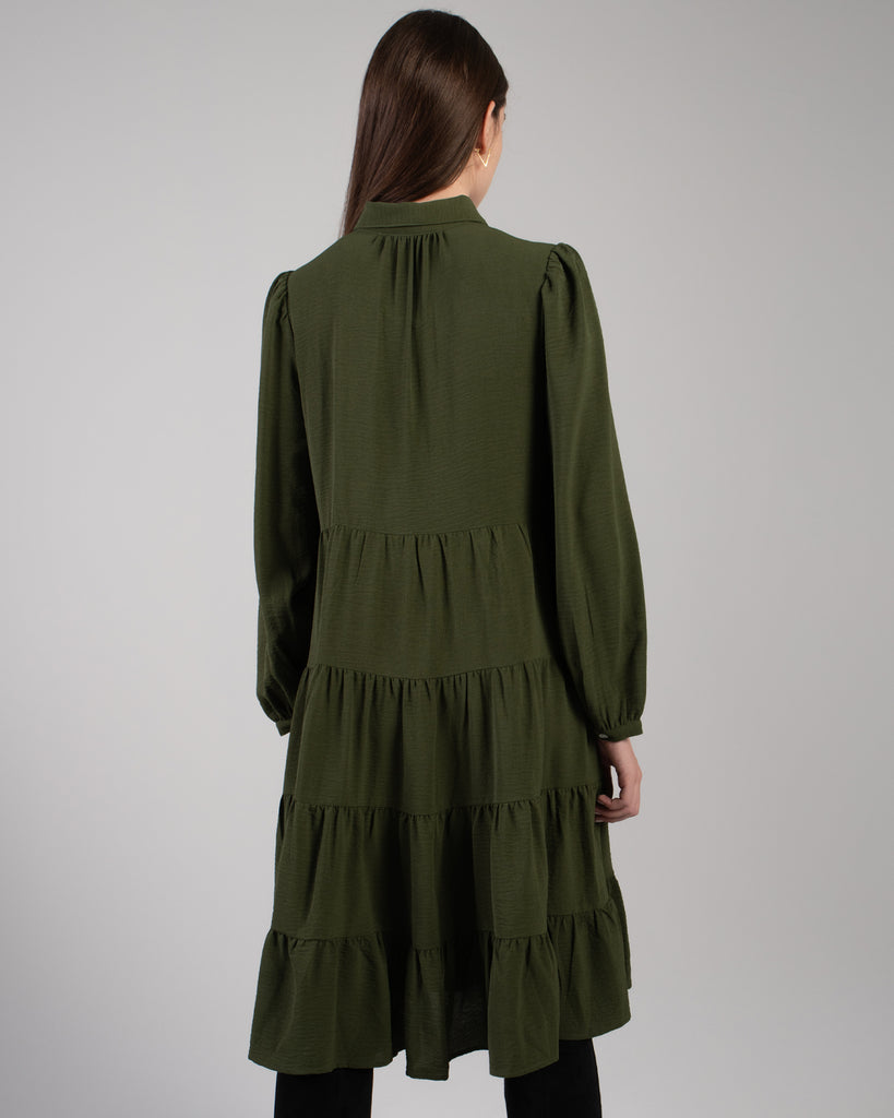 Back image of a model wearing a dark green long sleeve, knee-length dress with tiers.