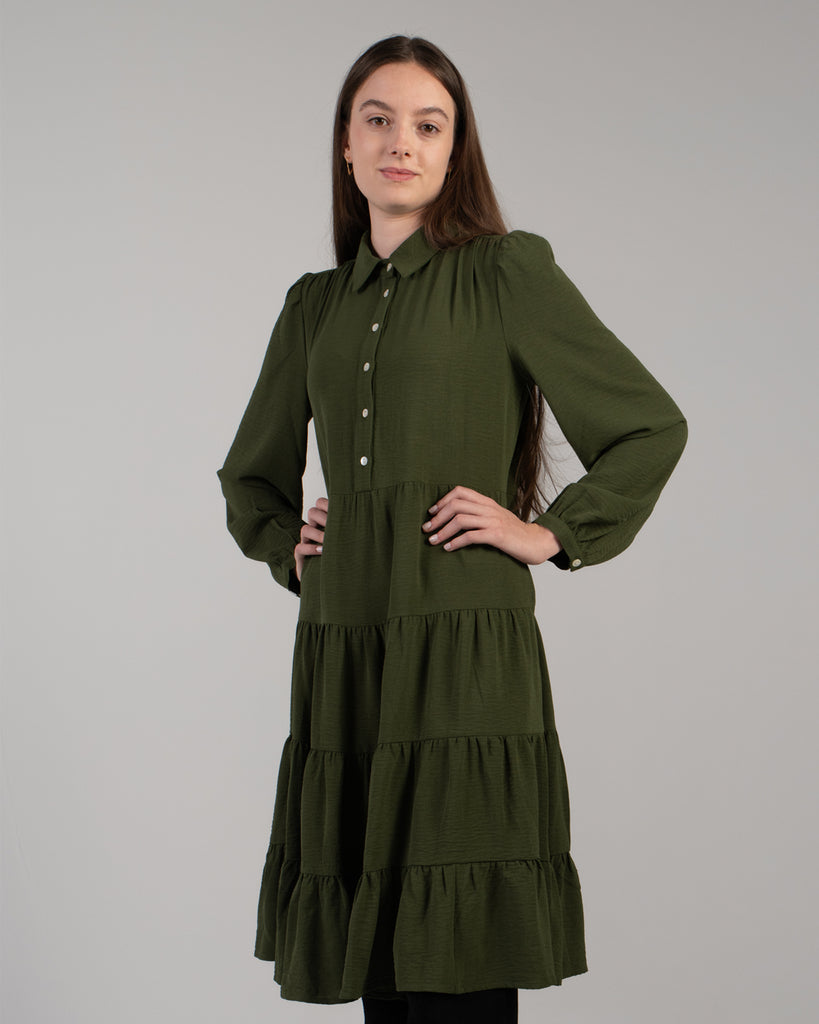 Model wearing a dark green long sleeve, knee-length dress with tiers and buttons down the front.