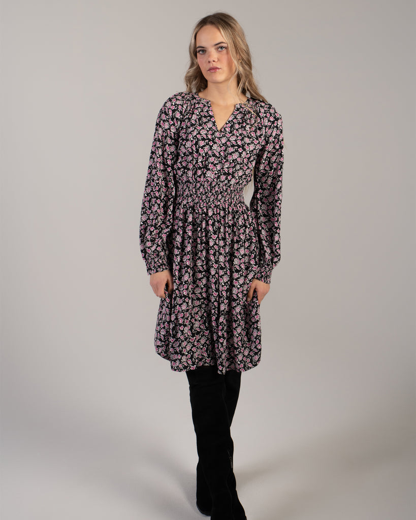 Woman in a black with pink floral print dress that has long sleeves and is knee-length