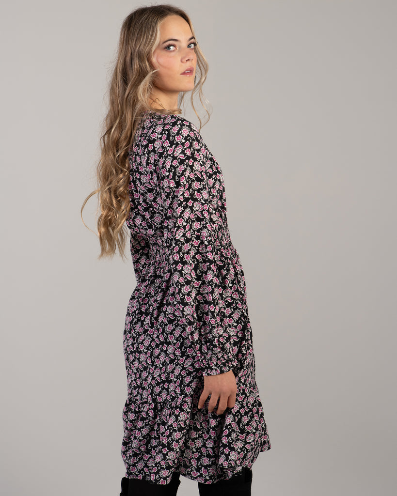 Woman in a black with pink floral print dress that has long sleeves and is knee-length