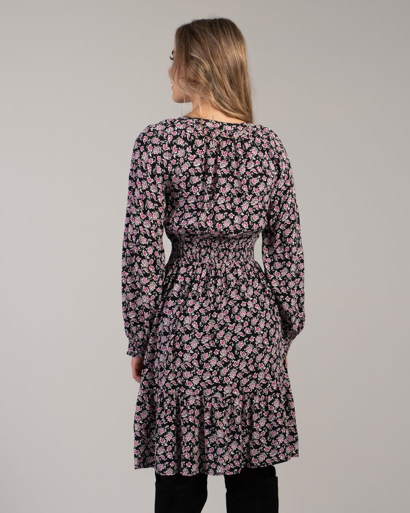 Woman in a black with pink floral print dress that has long sleeves and is knee-length