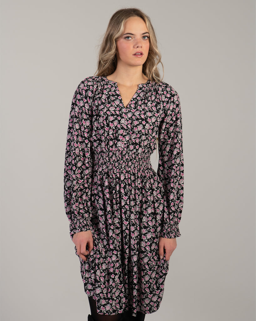 Woman in a black with pink floral print dress that has long sleeves and is knee-length