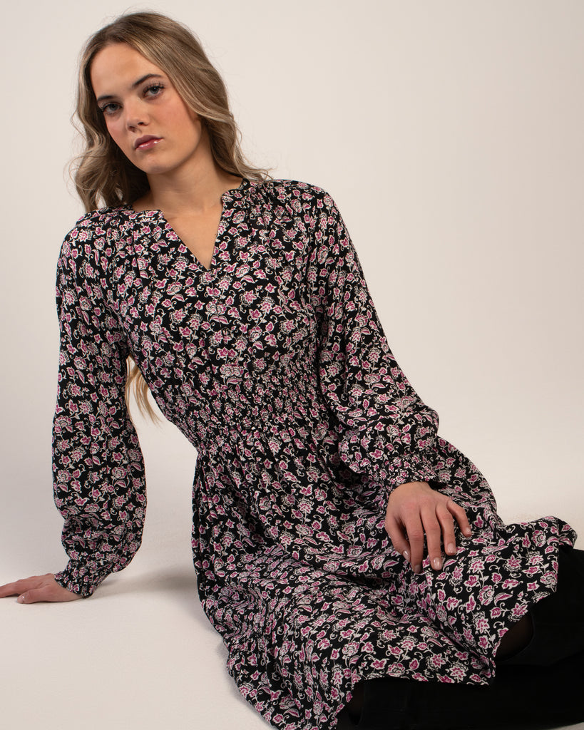 Woman in a black with pink floral print dress that has long sleeves and is knee-length