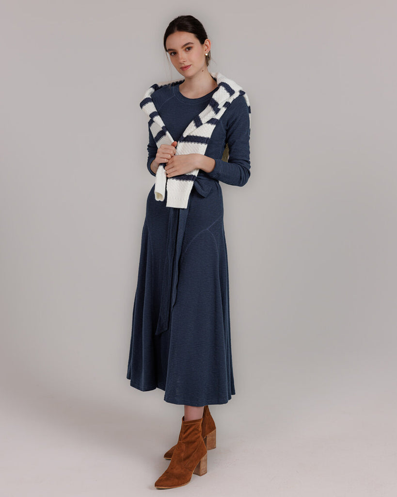 Model wearing a blue knit long sleeve fit and flare style dress that is midi length.