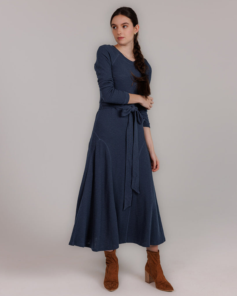 Model wearing a blue knit long sleeve fit and flare style dress that is midi length.