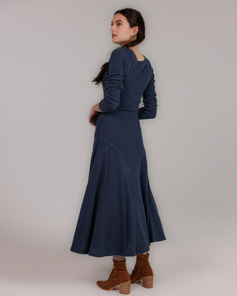 Model wearing a blue knit long sleeve fit and flare style dress that is midi length.