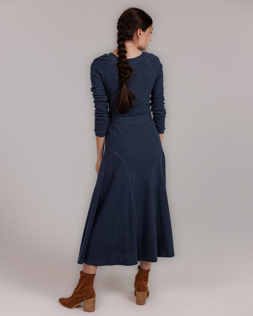 Model wearing a blue knit long sleeve fit and flare style dress that is midi length.