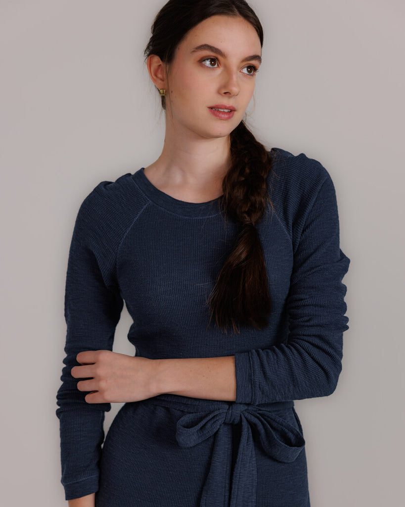 Model wearing a blue knit long sleeve fit and flare style dress that is midi length.