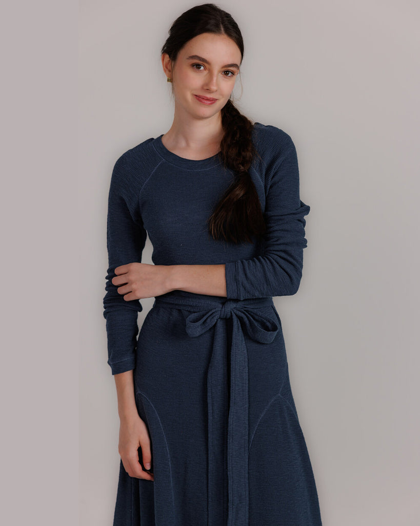 Model wearing a blue knit long sleeve fit and flare style dress that is midi length.