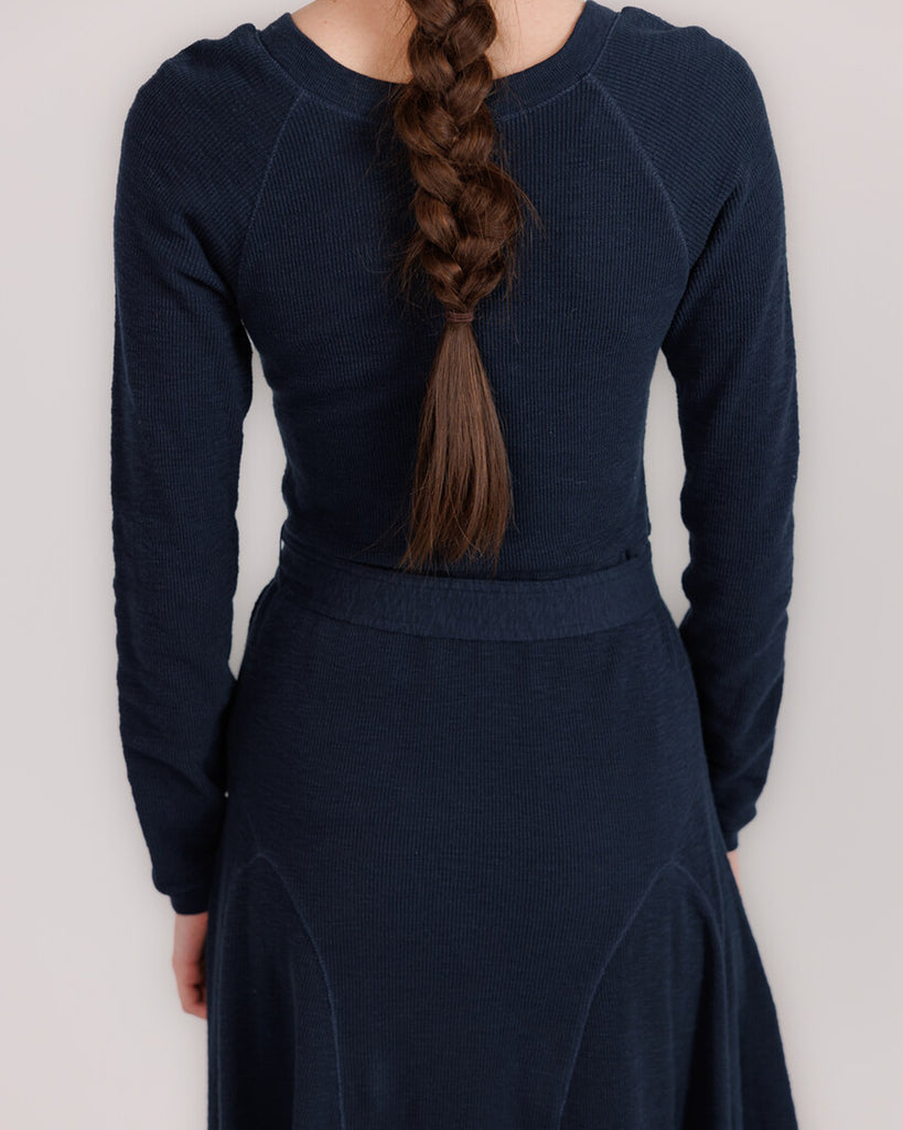 Model wearing a blue knit long sleeve fit and flare style dress that is midi length.