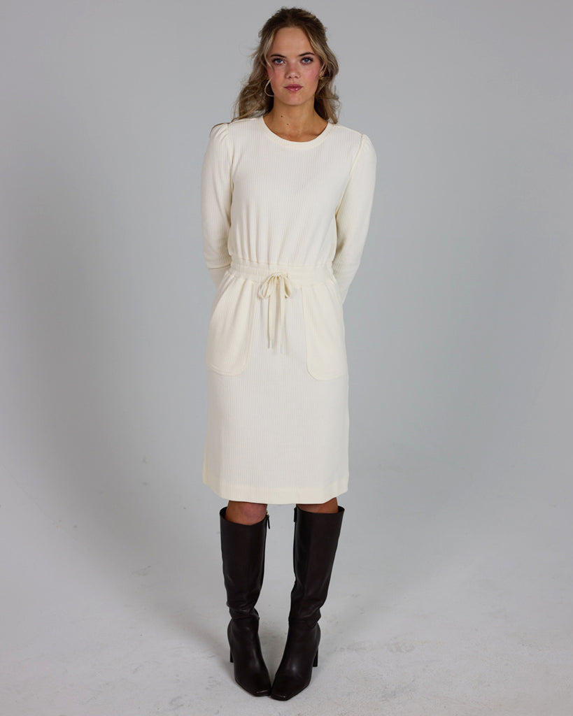 Model wearing a white long sleeve, round neck knee-length dress with a tie at the waist.