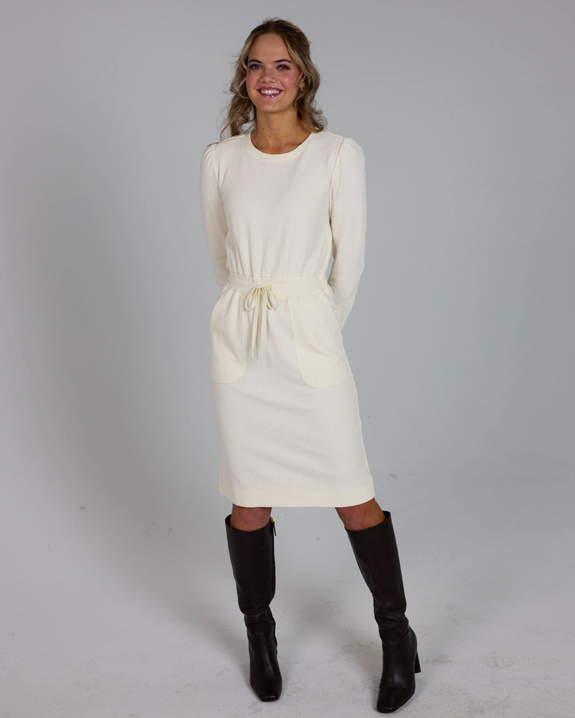 Model wearing a white long sleeve, round neck knee-length dress with a tie at the waist.