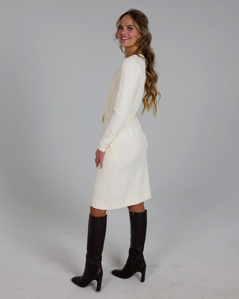 Model wearing a white long sleeve, round neck knee-length dress with a tie at the waist.