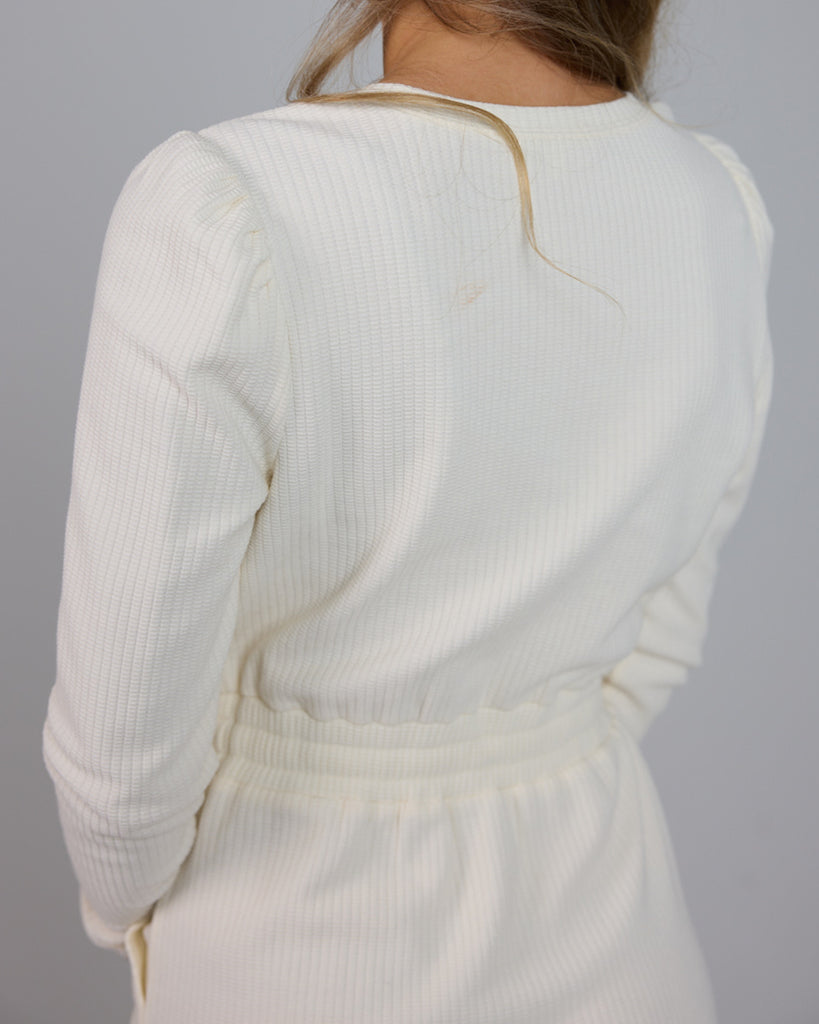 Model wearing a white long sleeve, round neck knee-length dress with a tie at the waist.