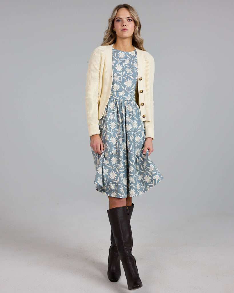 Model wearing a blue and white floral print, long sleeve, knee-length knit dress with pockets.