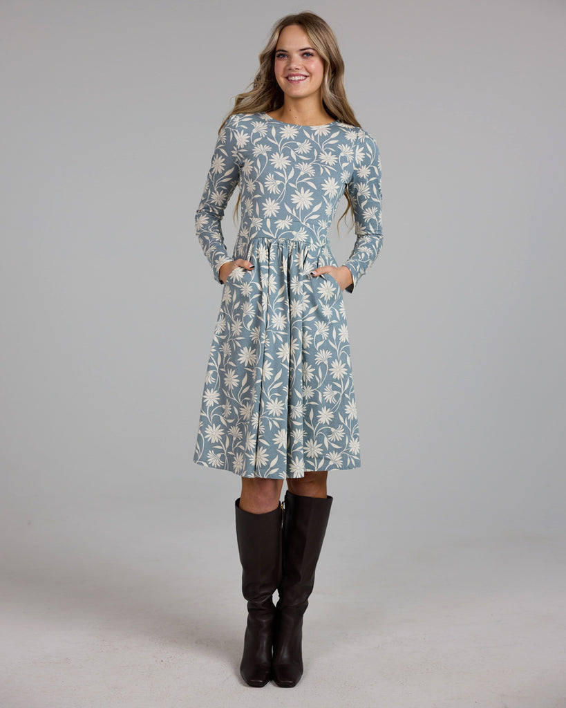 Model wearing a blue and white floral print, long sleeve, knee-length knit dress with pockets.