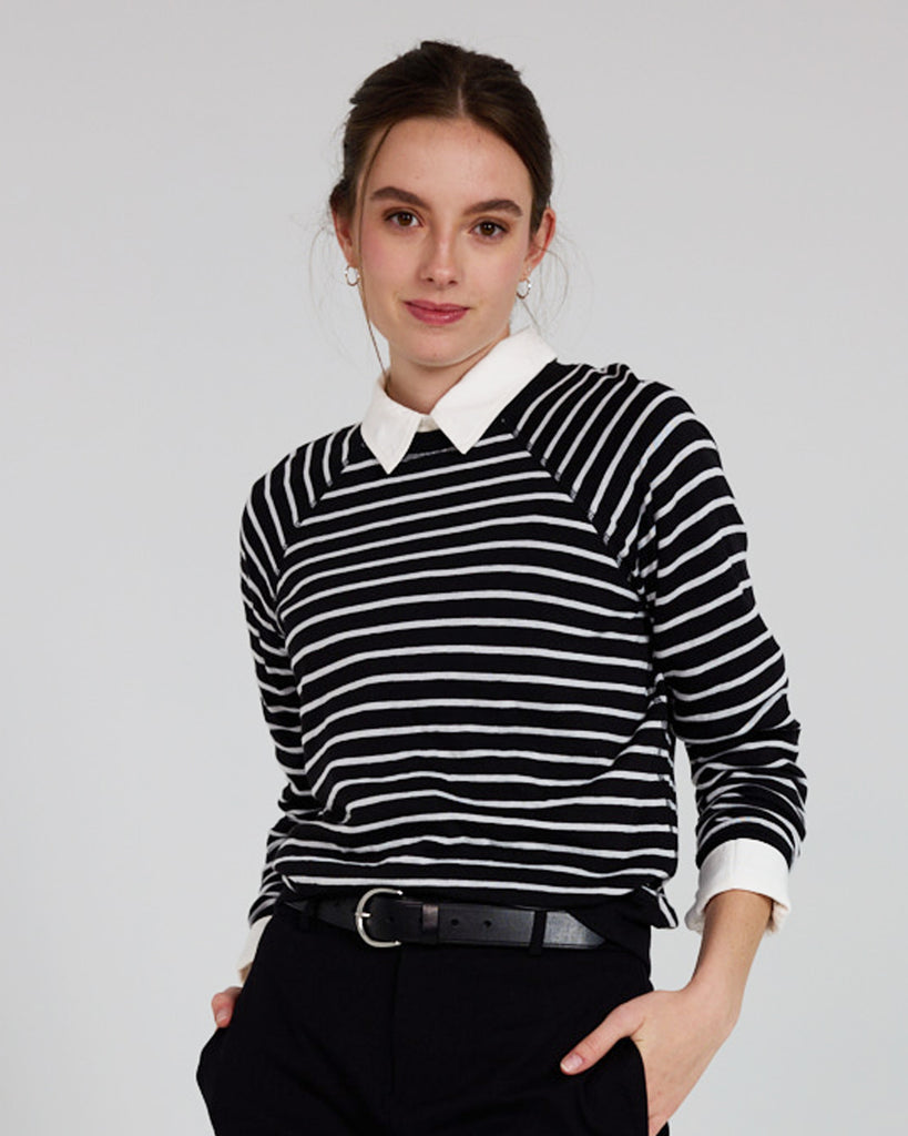 Model wearing a black and white stripe, long sleeve, crew neck with raglan seams pullover reversible sweater.