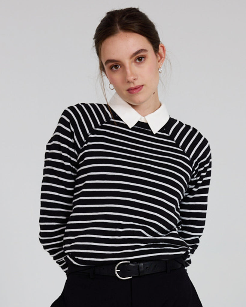 Model wearing a black and white stripe, long sleeve, crew neck with raglan seams pullover reversible sweater.