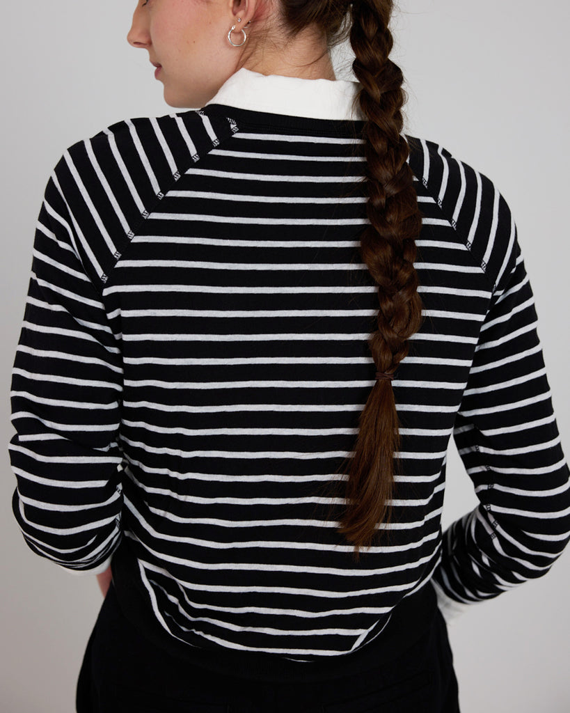 Model wearing a black and white stripe, long sleeve, crew neck with raglan seams pullover reversible sweater.