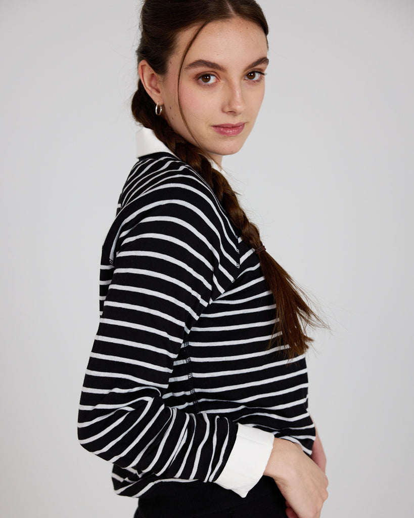 Model wearing a black and white stripe, long sleeve, crew neck with raglan seams pullover reversible sweater.