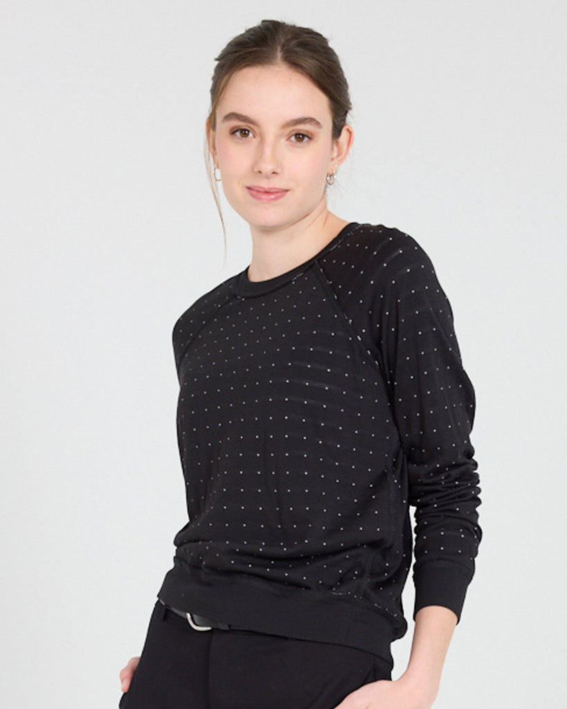 Model wearing a black with white polka dot, long sleeve, crew neck with raglan seams pullover reversible sweater.