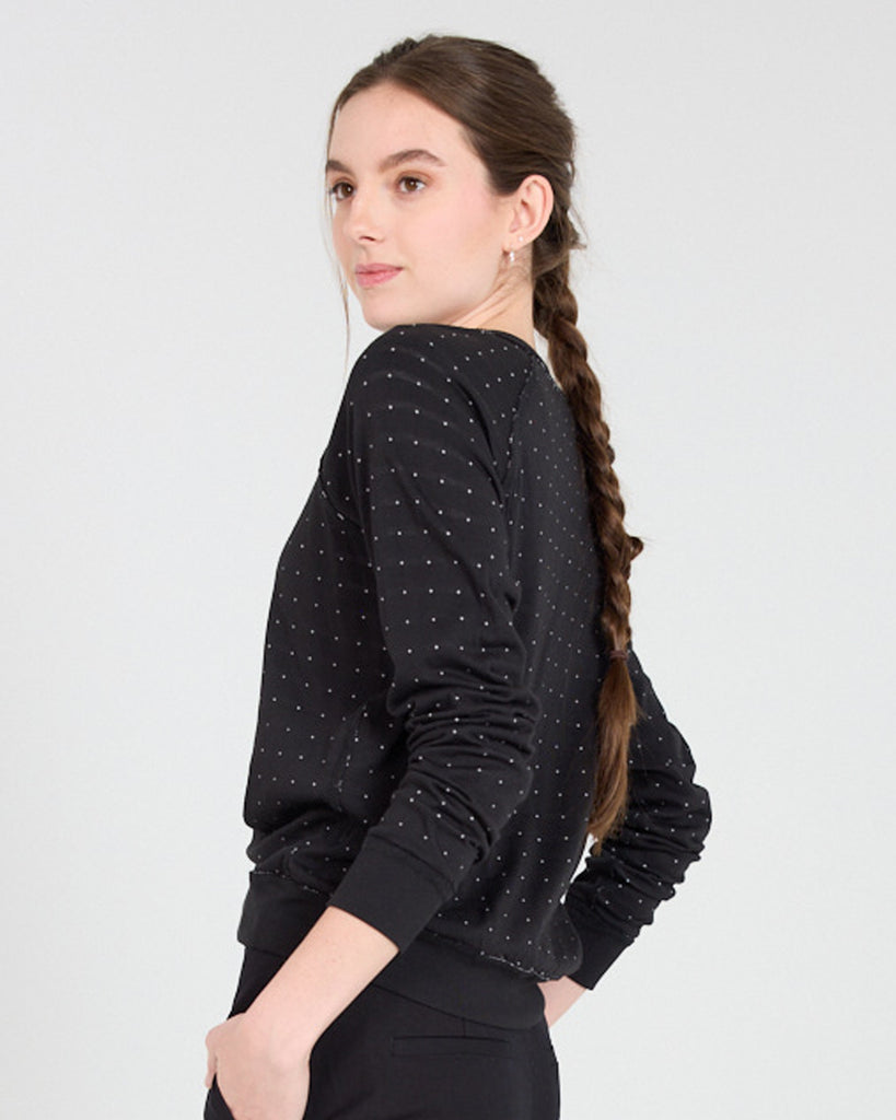 Model wearing a black with white polka dot, long sleeve, crew neck with raglan seams pullover reversible sweater.