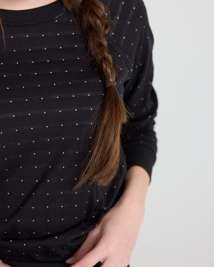 Model wearing a black with white polka dot, long sleeve, crew neck with raglan seams pullover reversible sweater.