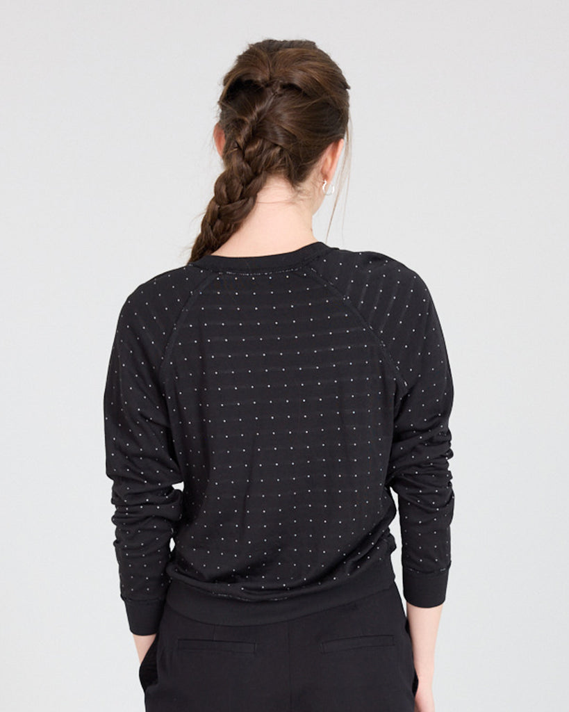 Model wearing a black with white polka dot, long sleeve, crew neck with raglan seams pullover reversible sweater.