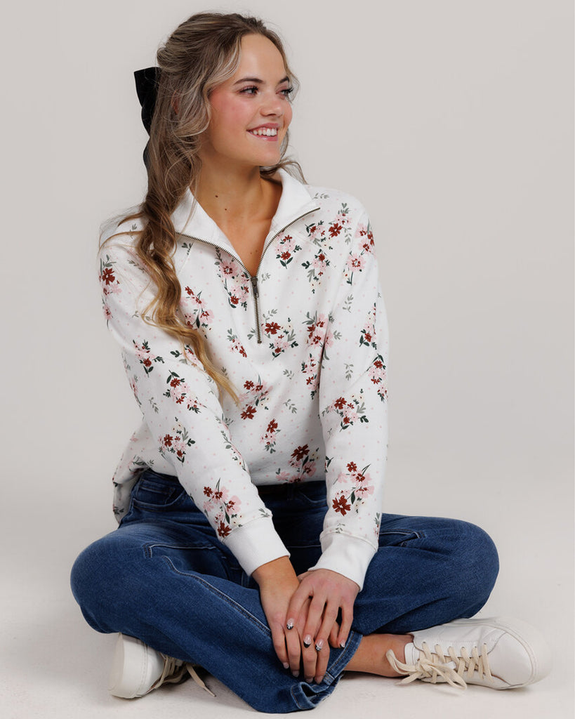 Model wearing a white with pink and red flowers, long sleeve, quarter zip sweatshirt.