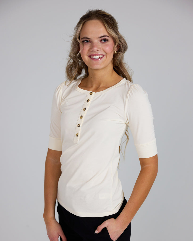 Model wearing a white half sleeve scoop neck henley top.