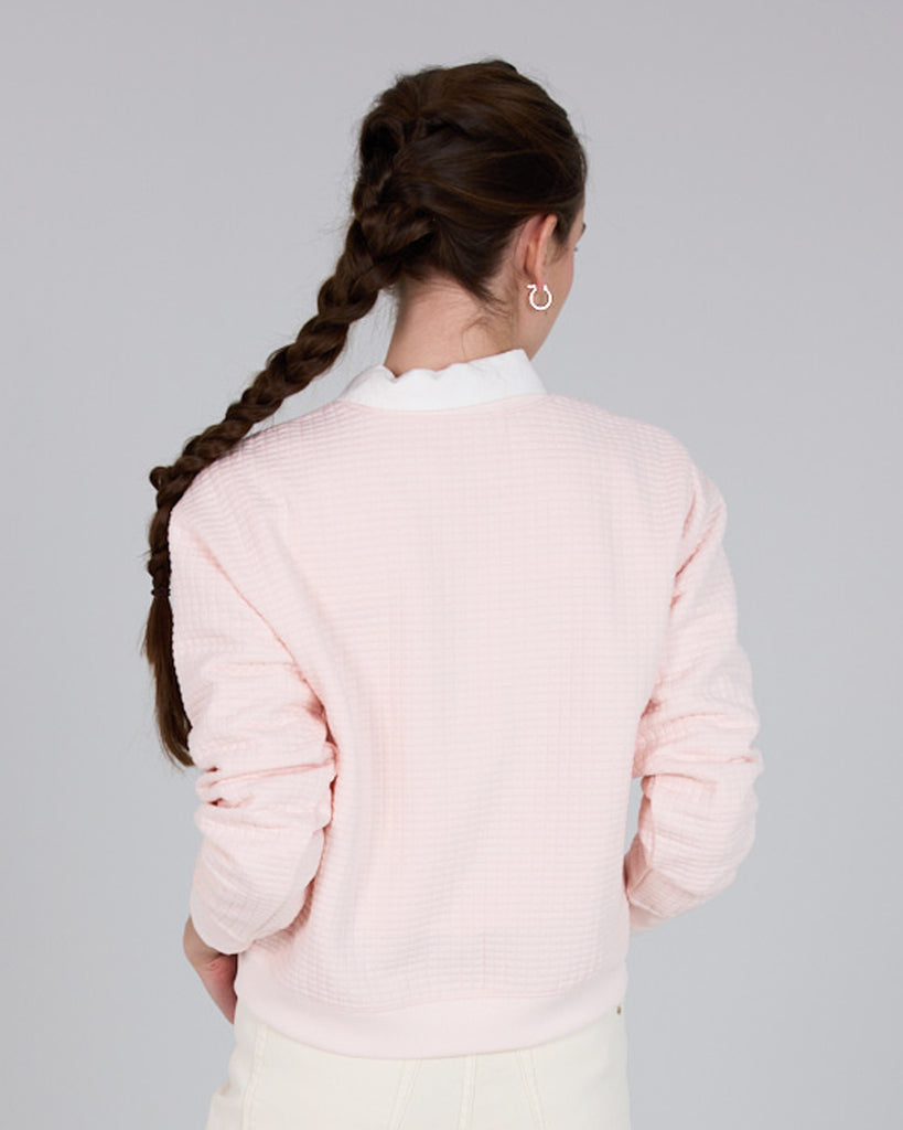 Model wearing a light pink, long sleeve, crew neck pullover sweater.