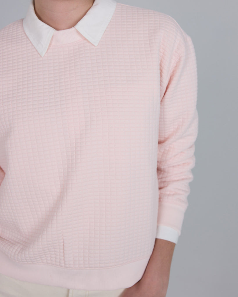 Model wearing a light pink, long sleeve, crew neck pullover sweater.