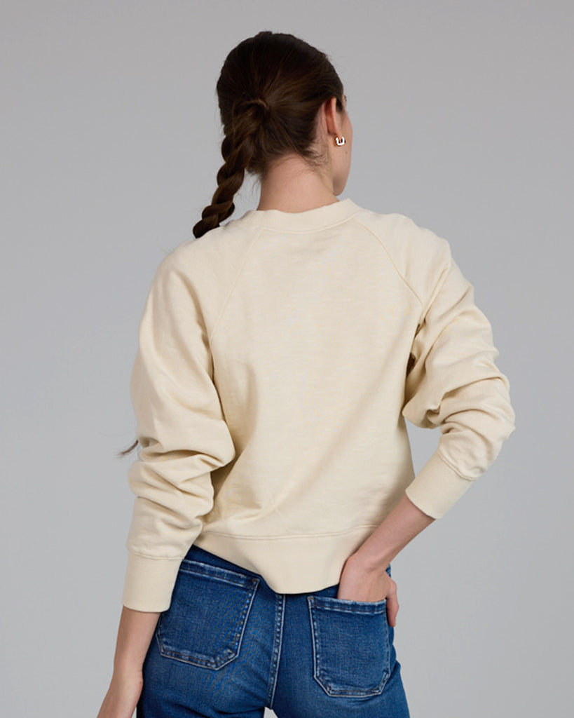 Model wearing an off-white with a blue heart print on the front, long sleeve crew neck sweatshirt.