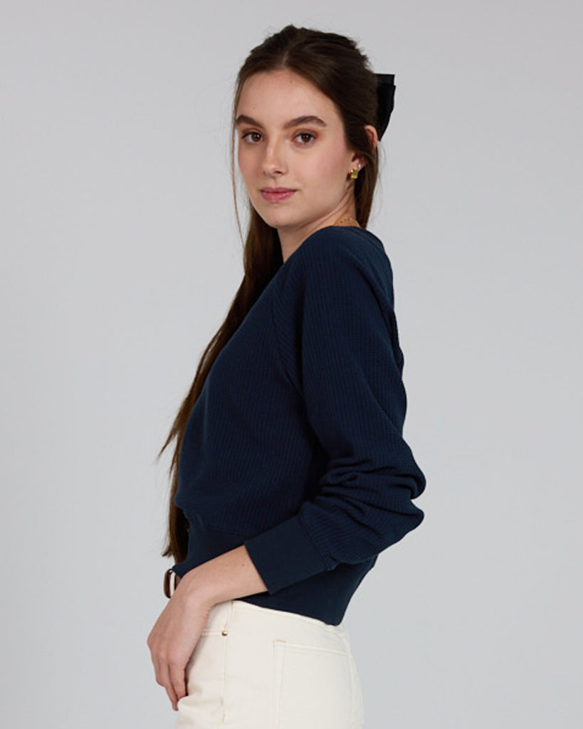 Model wearing a dark blue, v-neck, long sleeve waffle fabric pullover sweater.