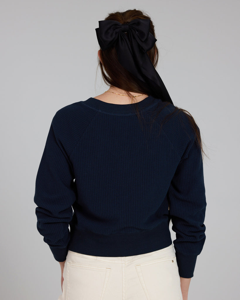 Model wearing a dark blue, v-neck, long sleeve waffle fabric pullover sweater.