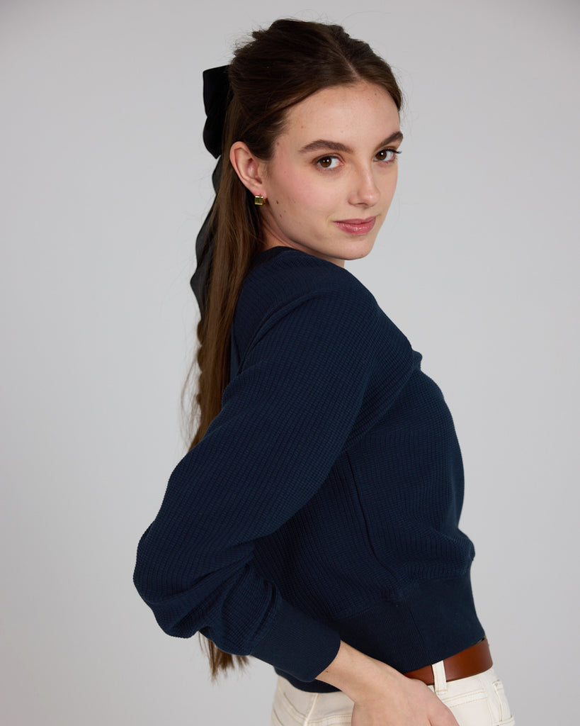 Model wearing a dark blue, v-neck, long sleeve waffle fabric pullover sweater.